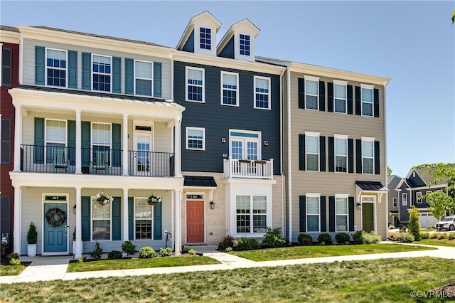 view of property featuring a porch, a balcony, and a front lawn