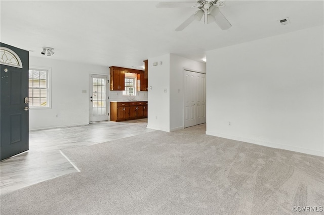 unfurnished living room featuring ceiling fan, light colored carpet, baseboards, and a sink