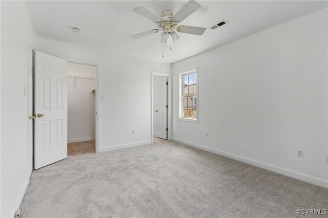 unfurnished bedroom featuring carpet flooring, baseboards, a walk in closet, and ceiling fan