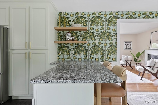 3454 Warner Rd, Richmond, VA 23225 - kitchen featuring wallpapered walls, a breakfast bar, dark stone counters, wood finished floors, and baseboards