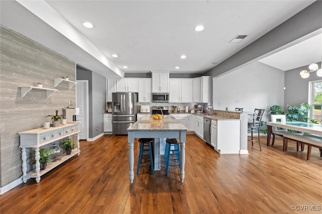 kitchen with a kitchen bar, white cabinets, light stone counters, a sink, and appliances with stainless steel finishes