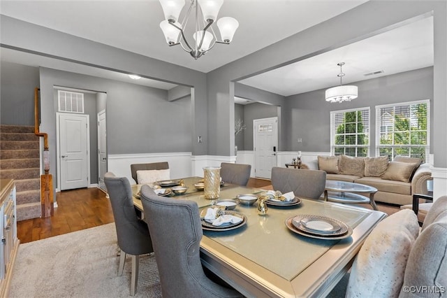 dining area with visible vents, wainscoting, wood finished floors, stairway, and an inviting chandelier