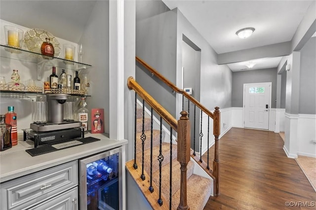 bar featuring wainscoting, wood finished floors, a bar, wine cooler, and stairs