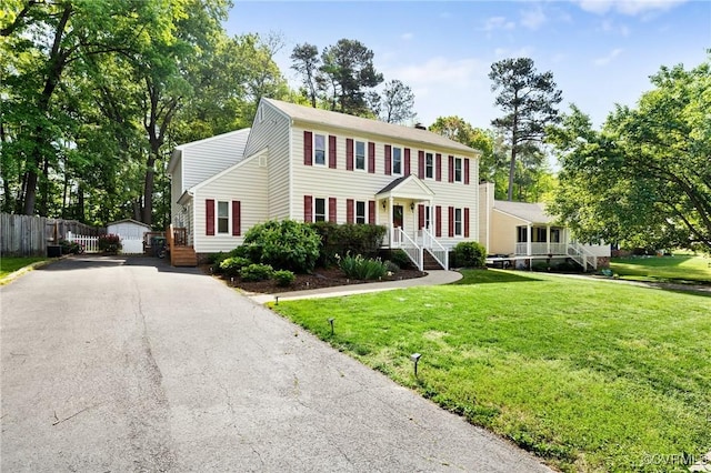 colonial home with fence, an outdoor structure, and a front lawn