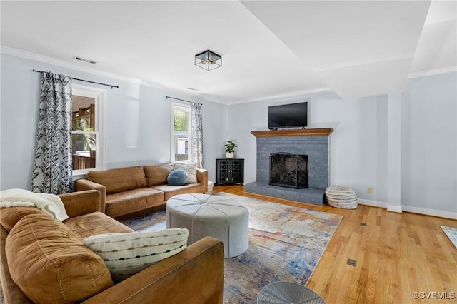 living area with visible vents, crown molding, a brick fireplace, wood finished floors, and baseboards
