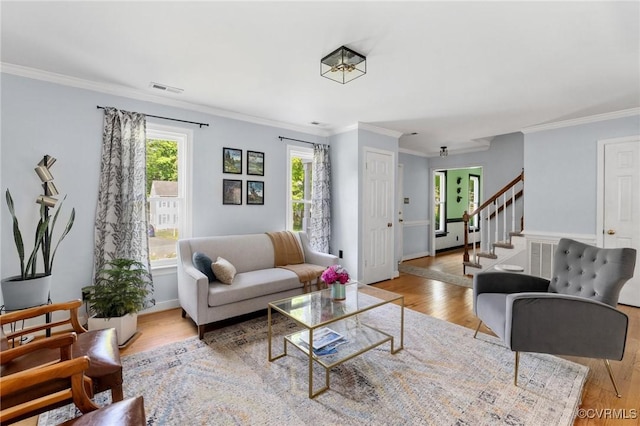living room with crown molding, visible vents, stairs, and light wood finished floors