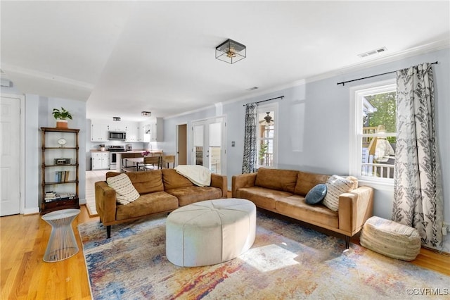 living room with visible vents, ornamental molding, and light wood-style floors