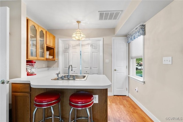 kitchen with visible vents, a peninsula, a breakfast bar, light countertops, and a sink