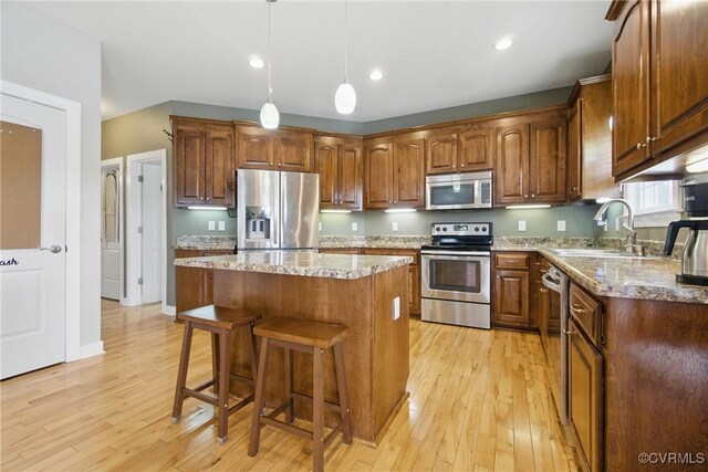 kitchen with stainless steel appliances, a kitchen breakfast bar, a sink, and light wood finished floors
