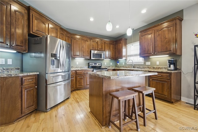 kitchen featuring a kitchen island, light wood-style floors, a breakfast bar area, a sink, and appliances with stainless steel finishes