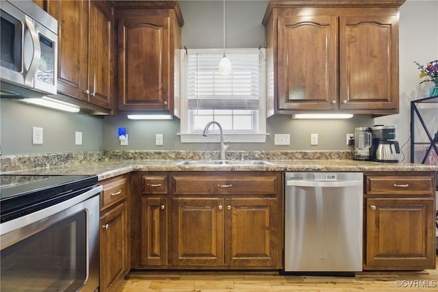 kitchen with a sink, light wood finished floors, appliances with stainless steel finishes, and light stone countertops
