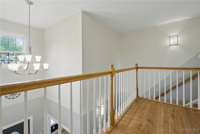 corridor featuring a notable chandelier, wood finished floors, and an upstairs landing