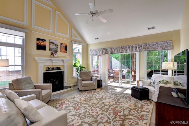 living room featuring a ceiling fan, visible vents, wood finished floors, high vaulted ceiling, and a fireplace with raised hearth