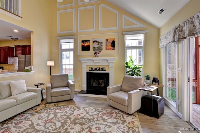 living area featuring visible vents, a fireplace with raised hearth, wood finished floors, and high vaulted ceiling