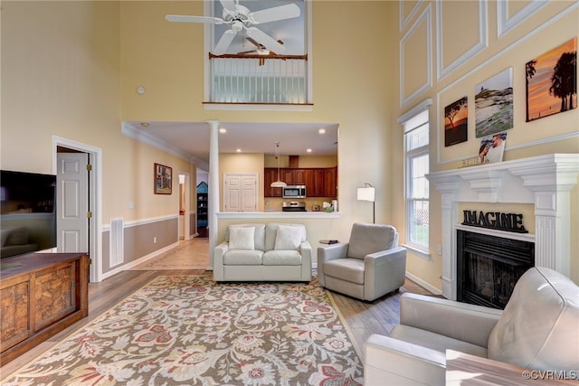 living area with a fireplace, a high ceiling, ceiling fan, and light wood-style floors