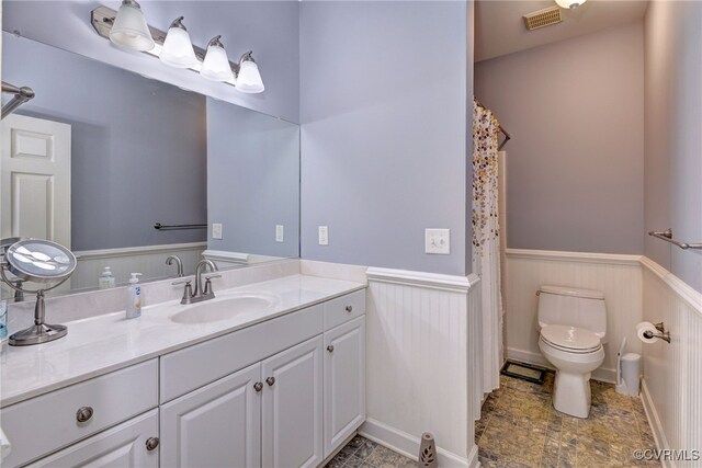 bathroom with vanity, toilet, a wainscoted wall, a shower with curtain, and visible vents