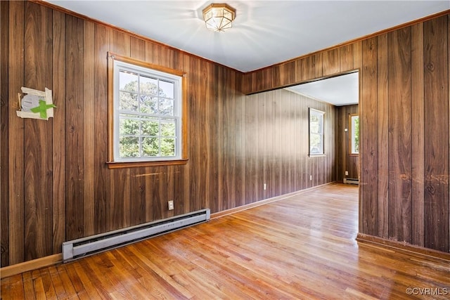 unfurnished room featuring wooden walls, wood finished floors, and baseboard heating