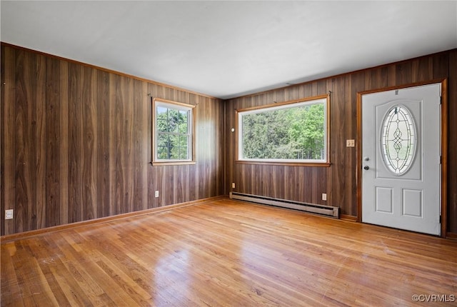 foyer entrance with wooden walls, a baseboard heating unit, and wood finished floors