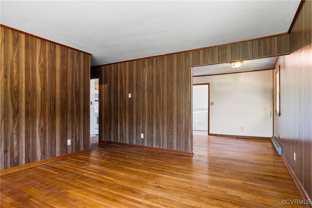 spare room featuring baseboard heating, wood walls, washer / clothes dryer, and wood finished floors
