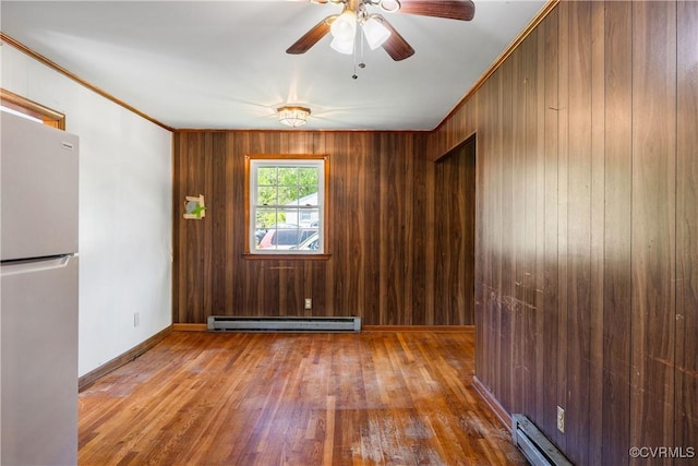 unfurnished room with wooden walls, ceiling fan, wood finished floors, and baseboard heating