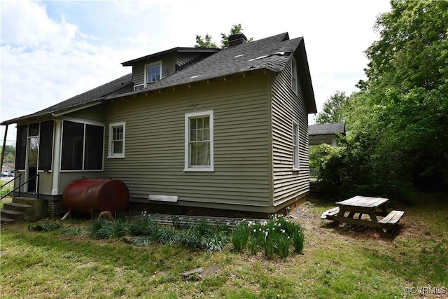 view of side of property featuring roof with shingles, a sunroom, entry steps, heating fuel, and a chimney