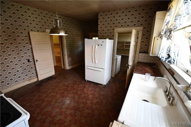 kitchen with decorative light fixtures, a sink, washer / dryer, wallpapered walls, and white appliances