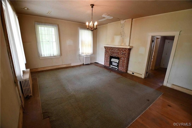 unfurnished living room with an inviting chandelier, a fireplace, baseboards, radiator heating unit, and dark wood finished floors