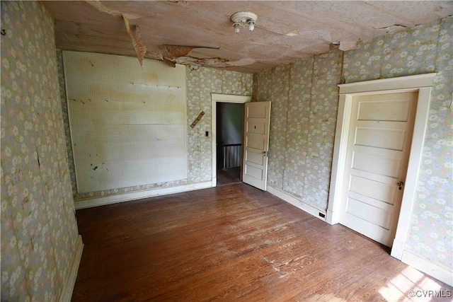 unfurnished room with baseboards, wallpapered walls, and wood finished floors