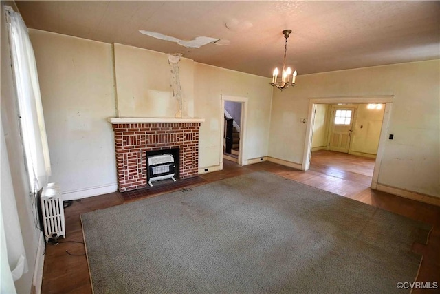 unfurnished living room featuring an inviting chandelier, baseboards, radiator, and wood finished floors