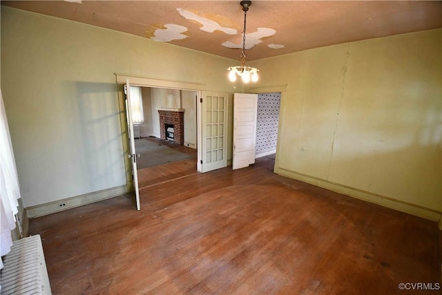 unfurnished dining area featuring an inviting chandelier, baseboards, a brick fireplace, and wood finished floors