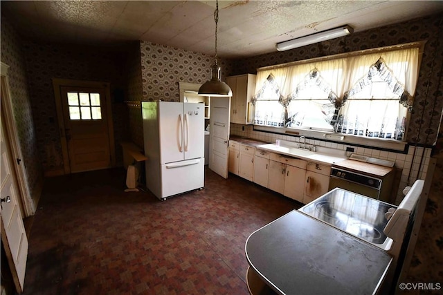 kitchen with hanging light fixtures, a sink, freestanding refrigerator, wallpapered walls, and dishwashing machine