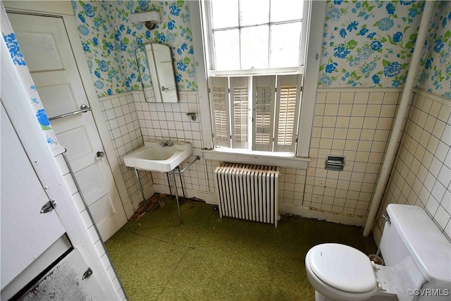 bathroom with radiator, a wainscoted wall, wallpapered walls, and tile walls