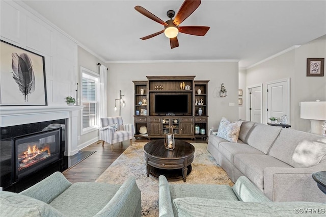 living room with ornamental molding, wood finished floors, ceiling fan, and a glass covered fireplace