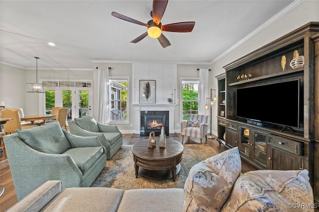living room featuring a ceiling fan, wood finished floors, a tiled fireplace, ornamental molding, and baseboards