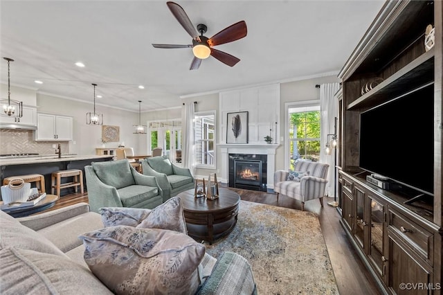 living area featuring dark wood-style flooring, ceiling fan, a fireplace, crown molding, and recessed lighting