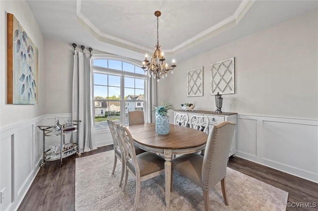 dining room featuring a chandelier, a raised ceiling, dark wood finished floors, a decorative wall, and ornamental molding