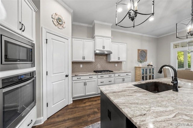 kitchen featuring appliances with stainless steel finishes, a chandelier, a sink, under cabinet range hood, and ornamental molding