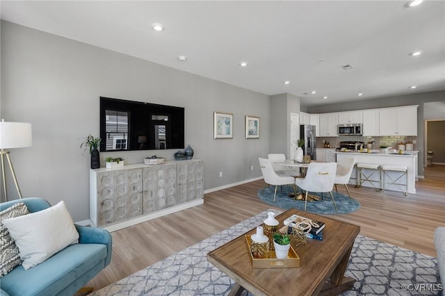 living room featuring recessed lighting, baseboards, and light wood finished floors
