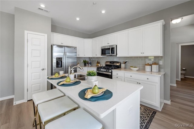kitchen with baseboards, white cabinets, a sink, appliances with stainless steel finishes, and backsplash