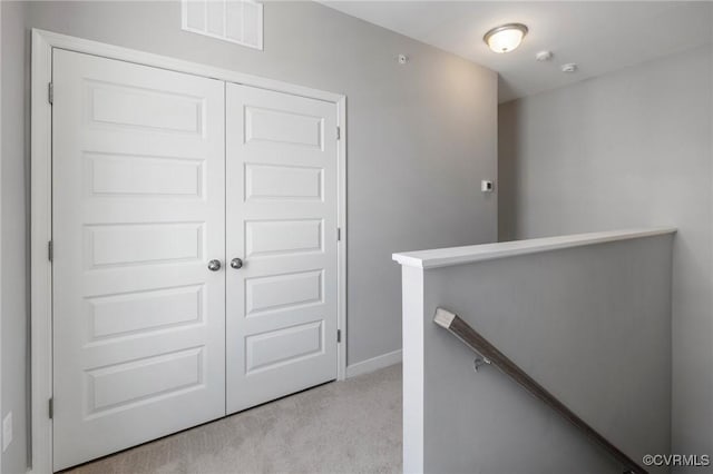 hall featuring visible vents, baseboards, an upstairs landing, and light colored carpet