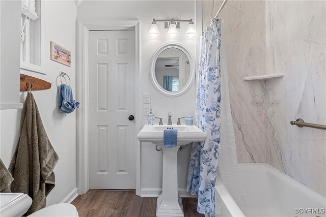 full bath featuring baseboards, wood finished floors, shower / bath combo, and toilet
