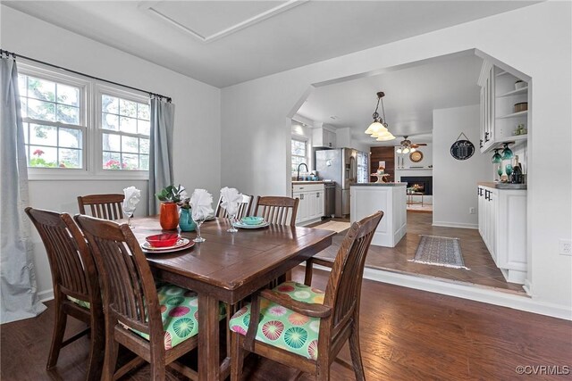 dining space featuring baseboards, arched walkways, wood finished floors, and a lit fireplace
