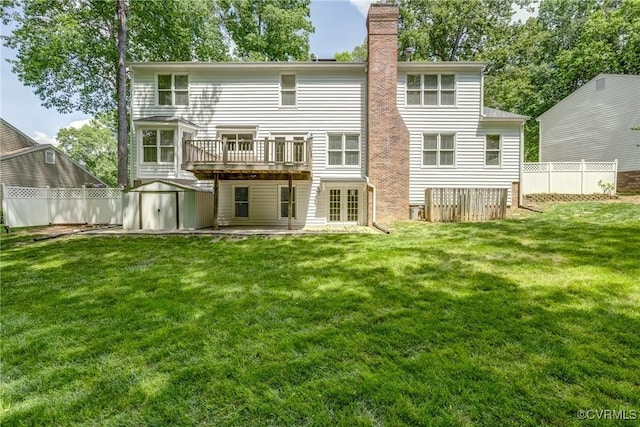 back of property featuring a wooden deck, a shed, a chimney, a lawn, and an outbuilding