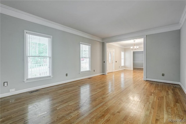 spare room with an inviting chandelier, ornamental molding, light wood finished floors, and baseboards