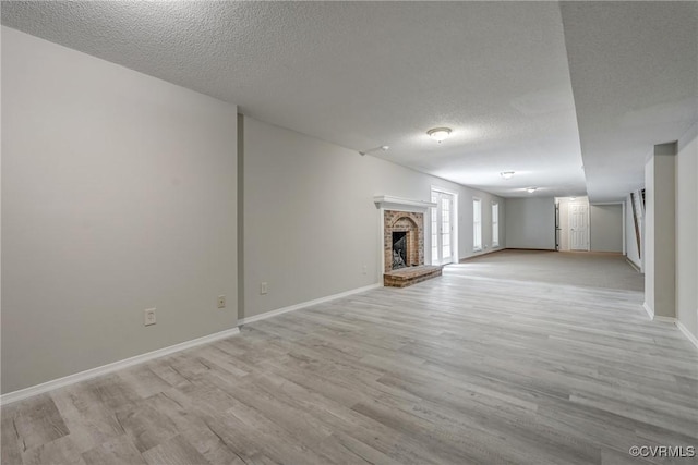 unfurnished living room with a textured ceiling, baseboards, light wood finished floors, and a fireplace