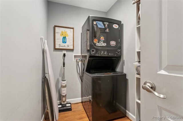 laundry area with baseboards, laundry area, stacked washing maching and dryer, and wood finished floors