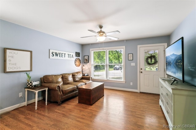 living area with baseboards, a ceiling fan, and wood finished floors
