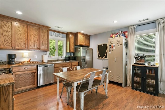 kitchen featuring brown cabinetry, visible vents, appliances with stainless steel finishes, light wood-type flooring, and a sink