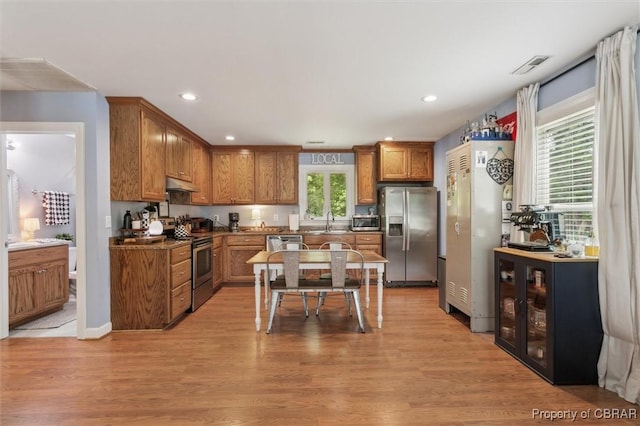 kitchen with brown cabinetry, visible vents, under cabinet range hood, a sink, and stainless steel appliances