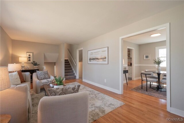 living room featuring baseboards, light wood-type flooring, and stairs